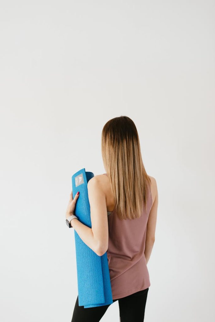 Rear view of a young woman holding a yoga mat, embodying a healthy and active lifestyle.